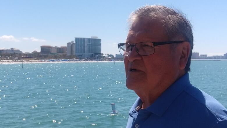 A man stands before a bright blue body of water.