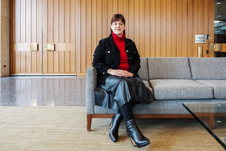 A woman in black and red sitting on a grey couch in the foyer at city hall.