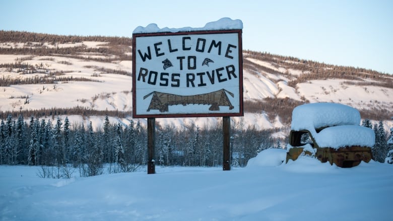 A welcome sign for the community of Ross River, Yukon. In the background are gently lit mountains.