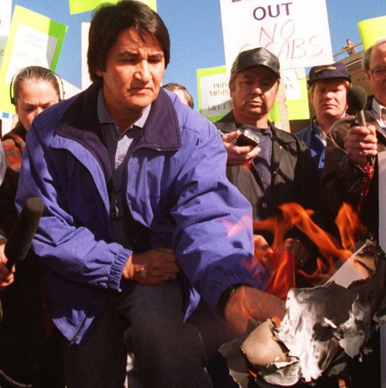 Onlookers watch as a kneeling man holds burning pieces of paper.