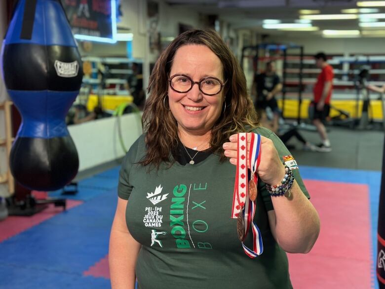 A woman in a boxing competition holds two bronze medals