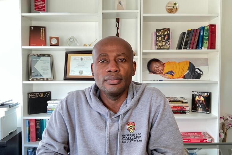 A man wearing a University of Calgary hoodie sits in an office.