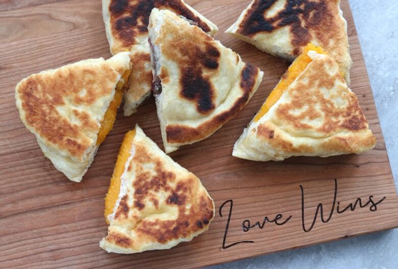 Crispy dough stuffed with potato and squash sits on a cutting board with love wins written on it.