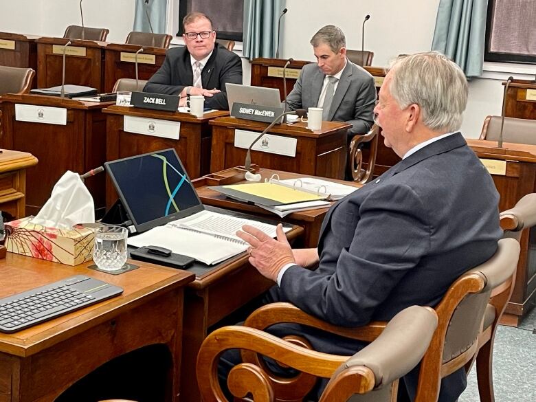 Derek Key sitting at wooden desk in PEI legislature, testifying to a legislative committee 