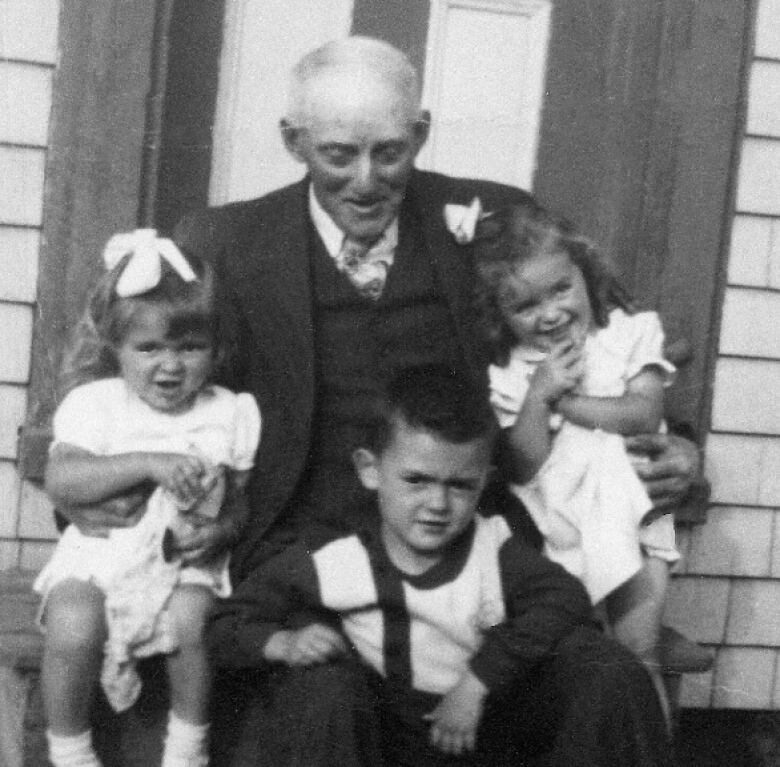 A black and white image of an elderly man in a suit surrounded by three young children.