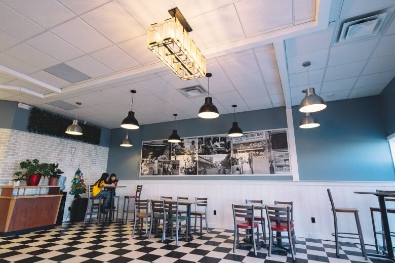 Two young girls sit at a table in the corner of an otherwise empty restaurant. It has black and white checkerboard tiles on the floor.