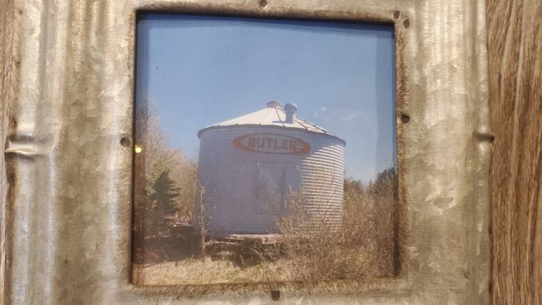 A framed photo of a steel silo standing above a tree line.