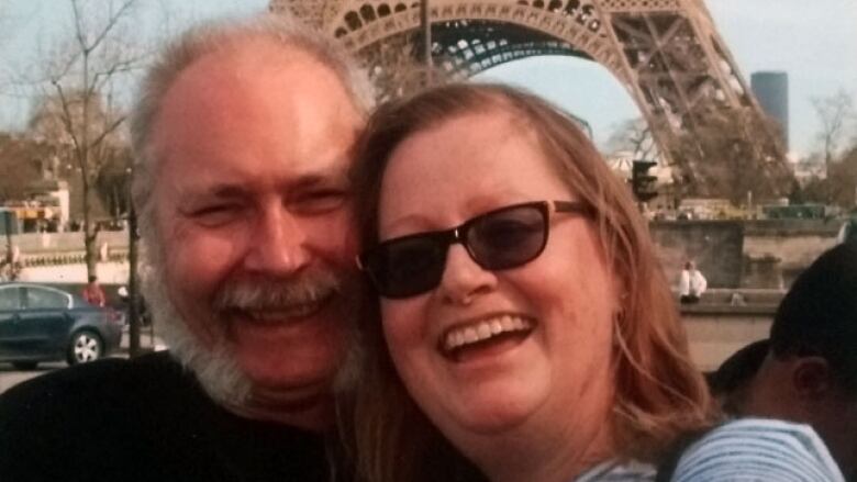 A man and woman smile in front of the Eiffel Tower.