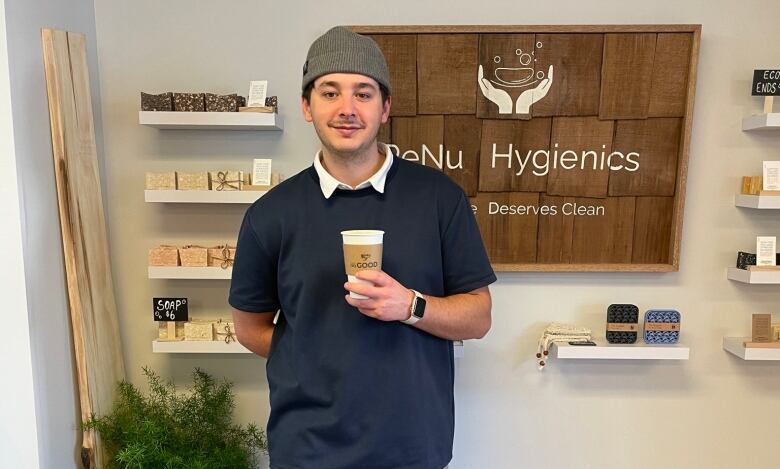 A man in a toque holds a togo coffee cup in front of a sign that says ReNu Hygienics.