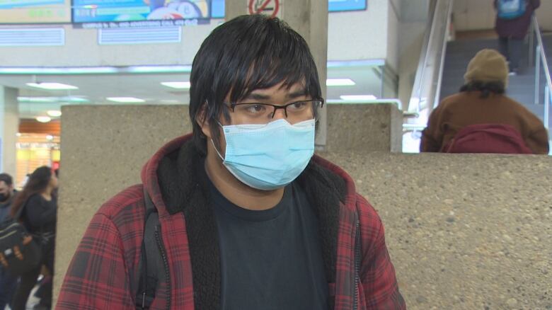 A man with glasses and a mask stands near a stiarwell.