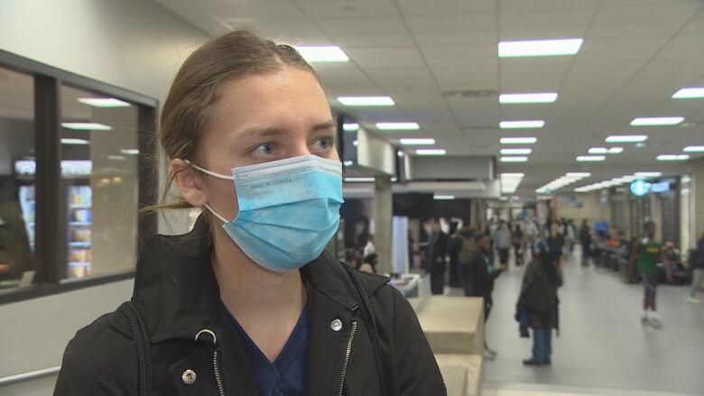 A woman with a mask stands in a hallway full of people.