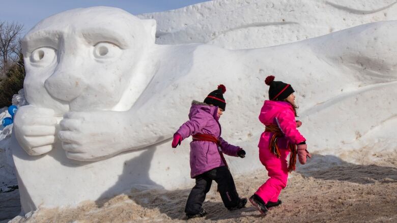 Children walk past a giant snow sculpture.