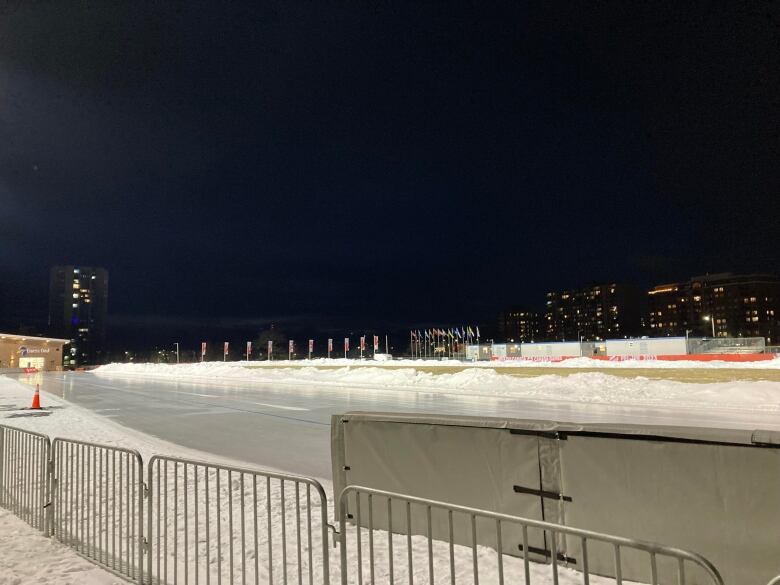 An ice skating rink, with a background showing a city skyline at night time.