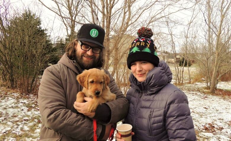 A couple stands outside on a winter day holding a golden retriever puppy.