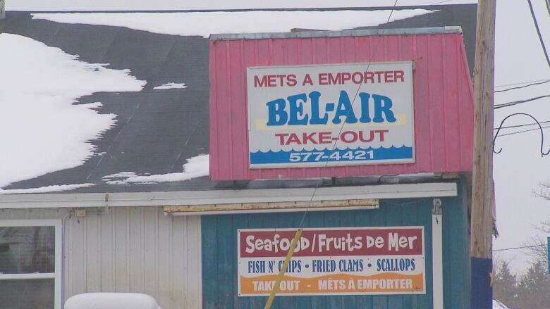 A blue and white building with a menu sign on the front, snow on the roof.