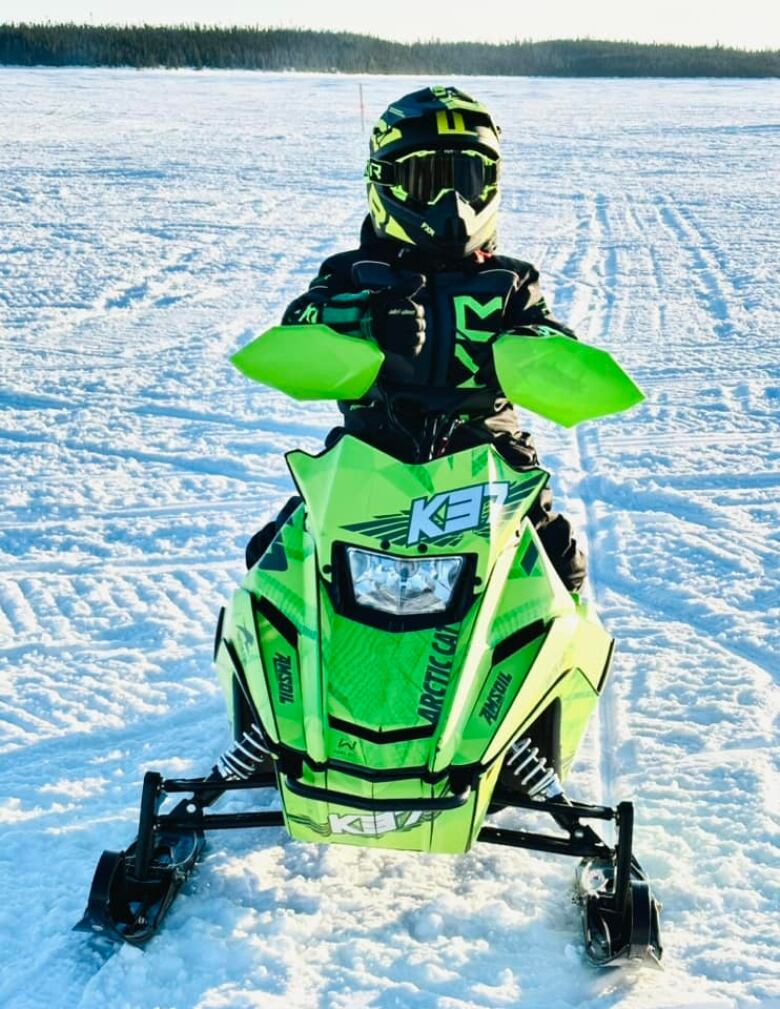 A young boy on a mini Arctic Cat snowmobile on a snowy lake.