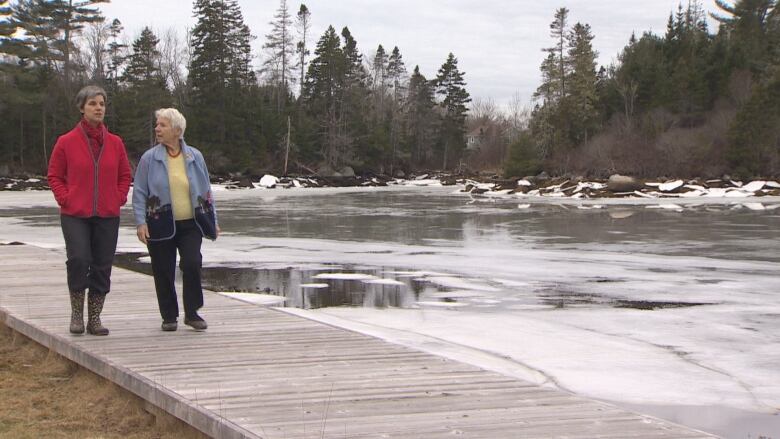 Two women walk on a boardwalk along the edge of the water.