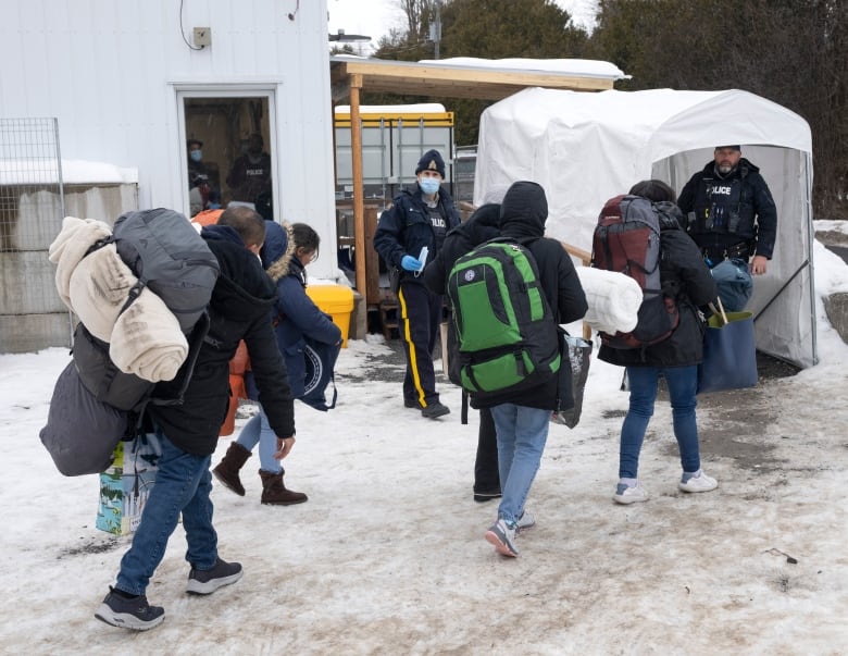 People in jackets walk towards police officers in the winter.