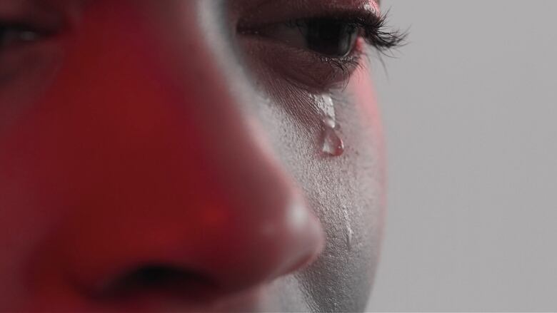 Close up of a face shows a tear rolling from an eye