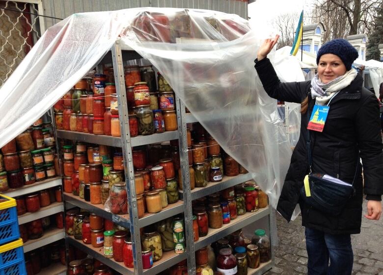 A woman stands next to a stand of canned vegetables.