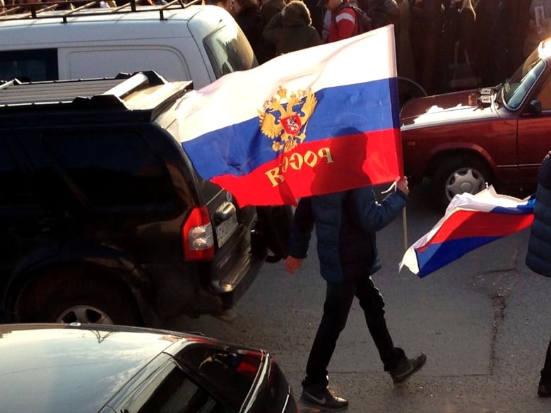 A person carries a Russian flag on a crowded street.