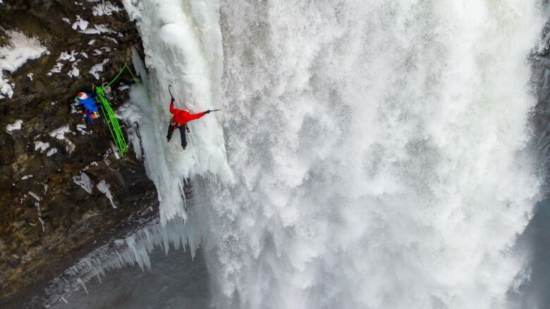 Wide shot of a man climbing a waterfall while the water is still flowing.