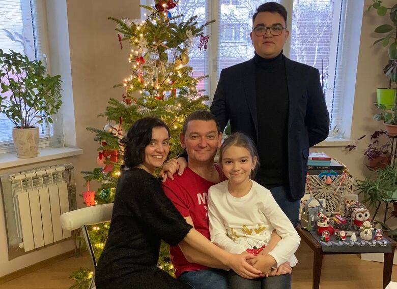 Four people pose in front of a Christmas tree.