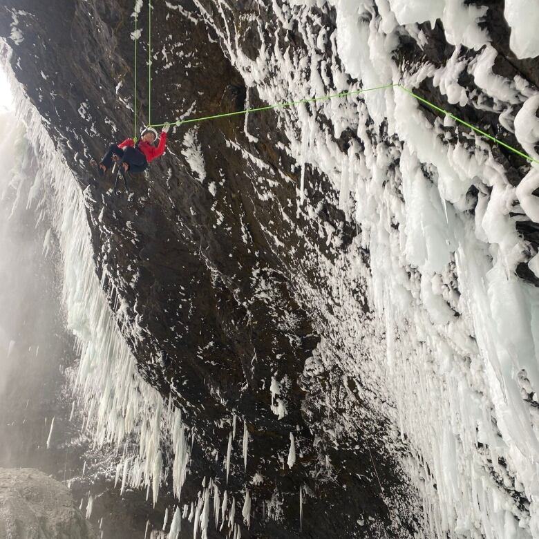 A man hangs off of a frozen waterfall.