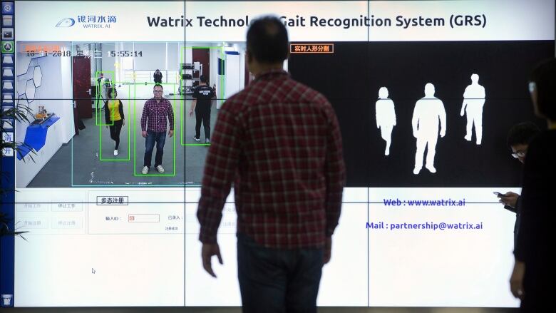 A man stands in front of a computer screen demonstrating recognition software. 