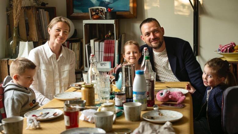 Mykhailo Pluzhnikov, his wife and three children are seated around a dining table having a meal and pose for a family portrait. 