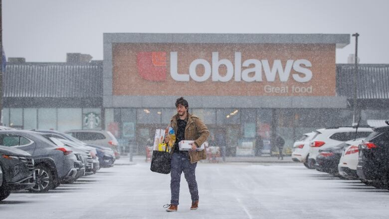 A man walks through a parking lot carrying groceries.