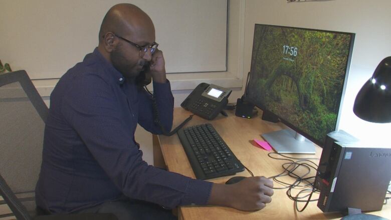 A man in a navy button-down answering the phone at his desk