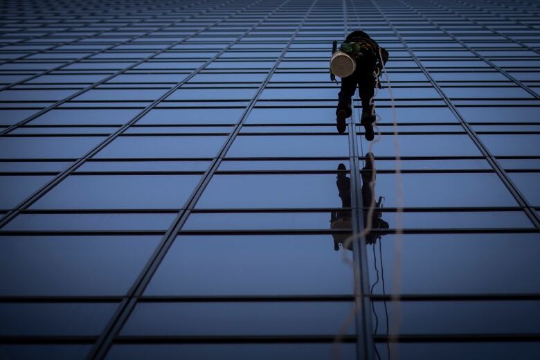 A window washer is pictured from below on a glass high-rise building.