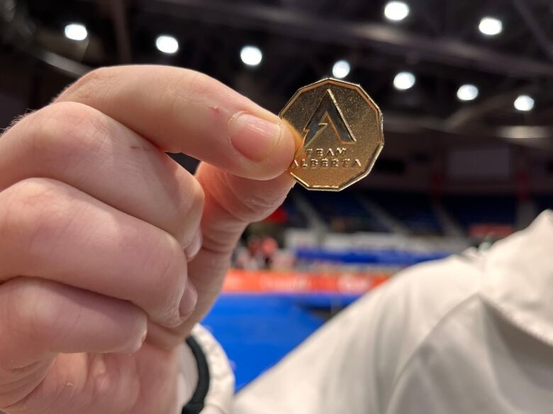 A close-up photo of someone holding a lucky loonie - a gold-coloured coin with Team Alberta written on it.