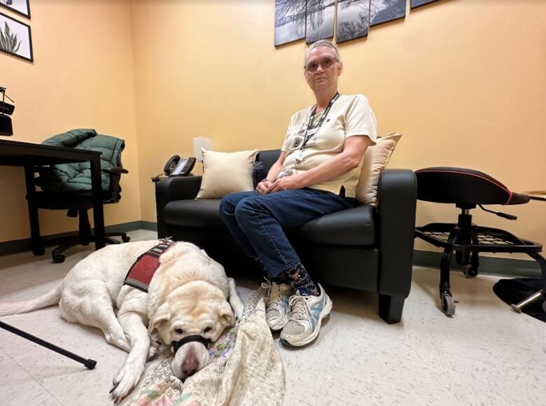 A woman sitting on the couch with her dog lying on the floor by her feet. 