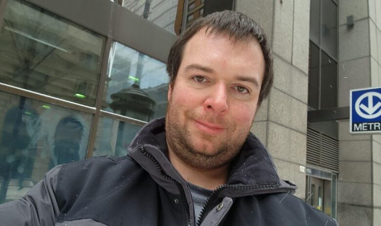 A man in a winter jacket stands outside a Metro station.