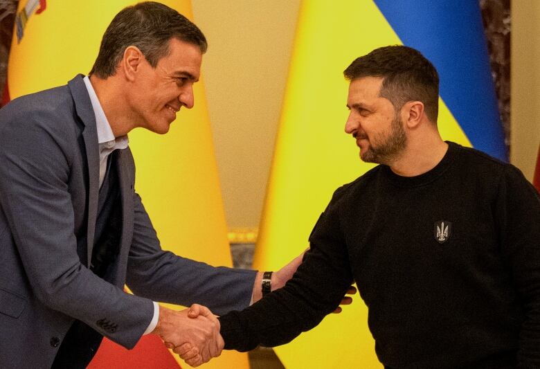 Two men shake hands before yellow flags seens behind them