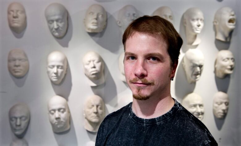 A man smiles in front of a wall of prosthetics.