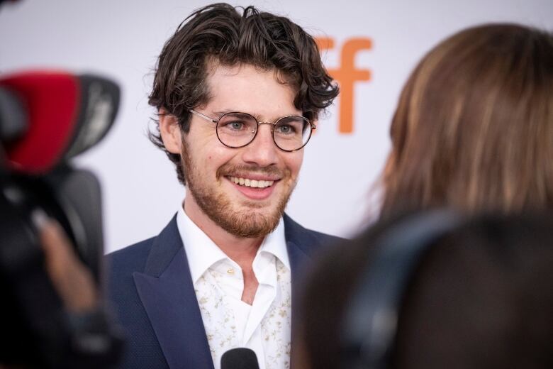 A man wearing glasses speaks to a reporter at an event.