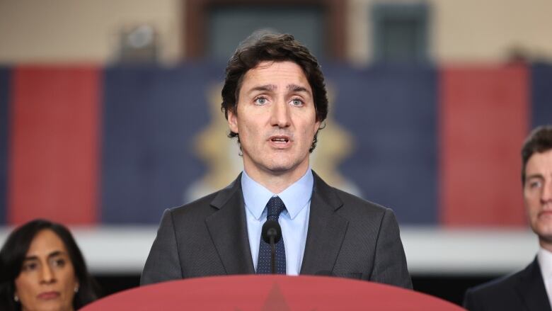 Prime Minister Justin Trudeau, wearing a suit and tie, stands at a podium making a speech.