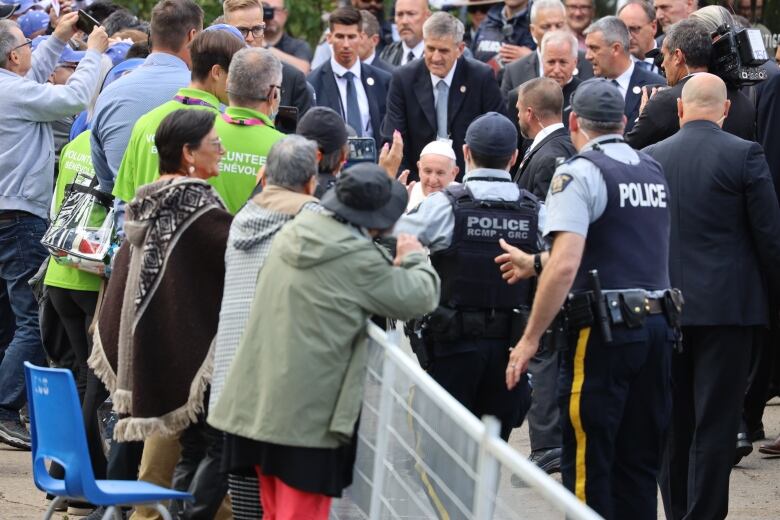 Mounties can be seen protecting Pope Francis as he makes an unscheduled visit to greet people on the other side of the barricade outside outside Sacred Heart Catholic Church of the First Peoples in Edmonton.