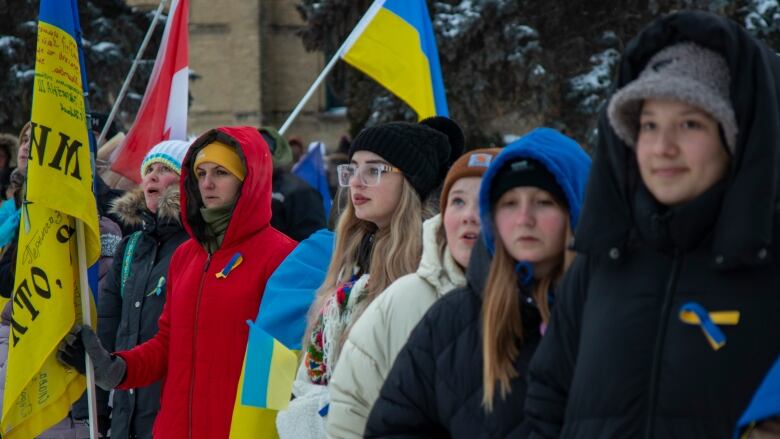 People in parkas hold blue and yellow Ukrainian flags outside.