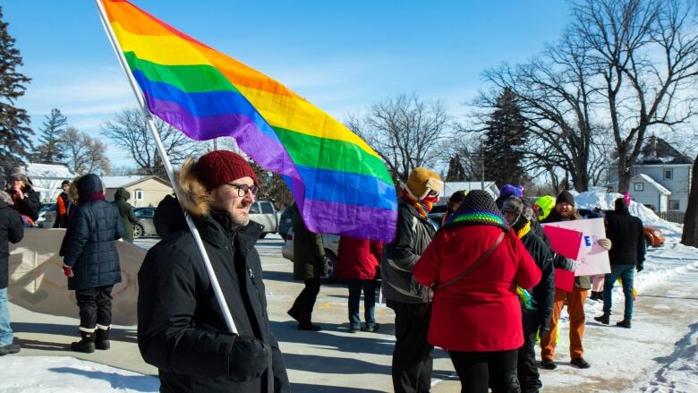 Ralliers dressed in winter gear hold pro LGBTQ signs.