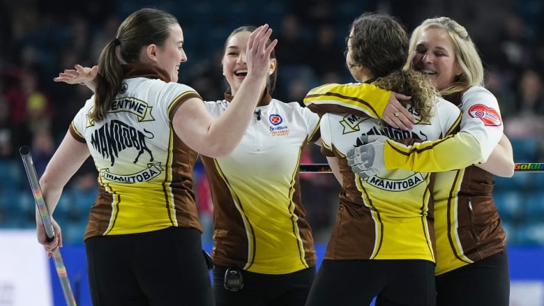 Four female curlers smile while hugging in celebration on the ice.