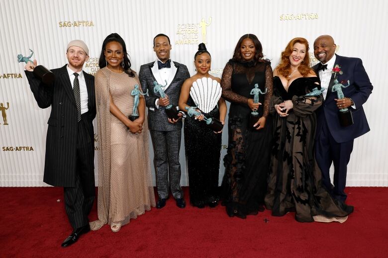 Actors pose for photographs with their awards on the red carpet.