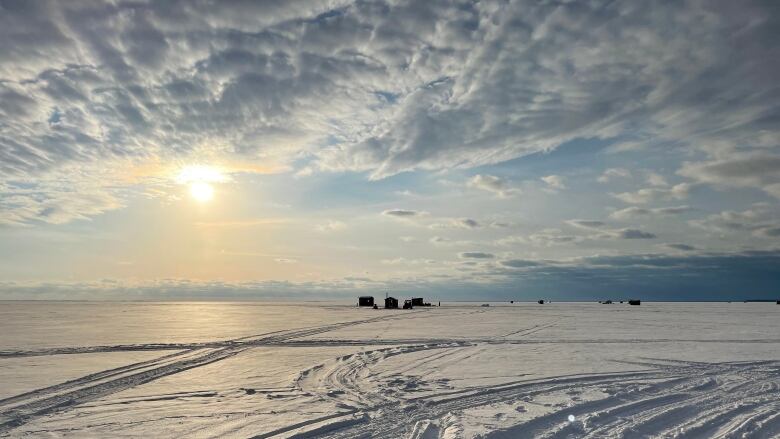 Ice fishing huts in a snowy lake near sunset.