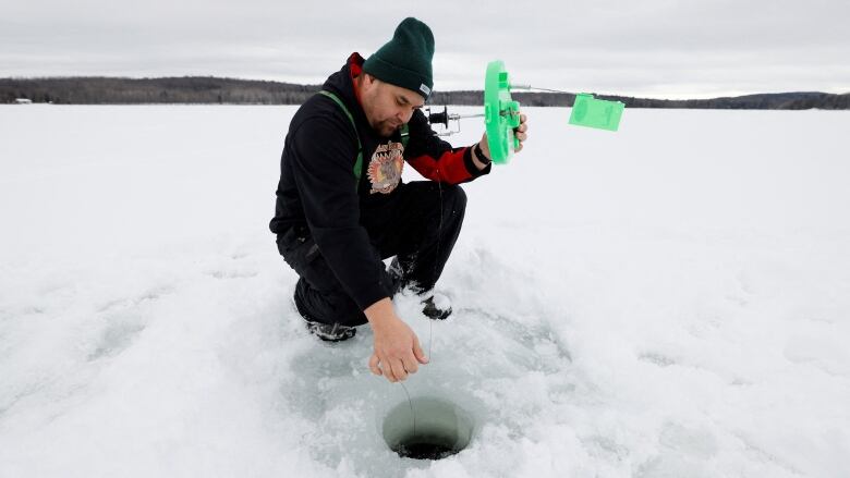 A fisher places a green lid-type ice fishing rig onto a hole in ice.