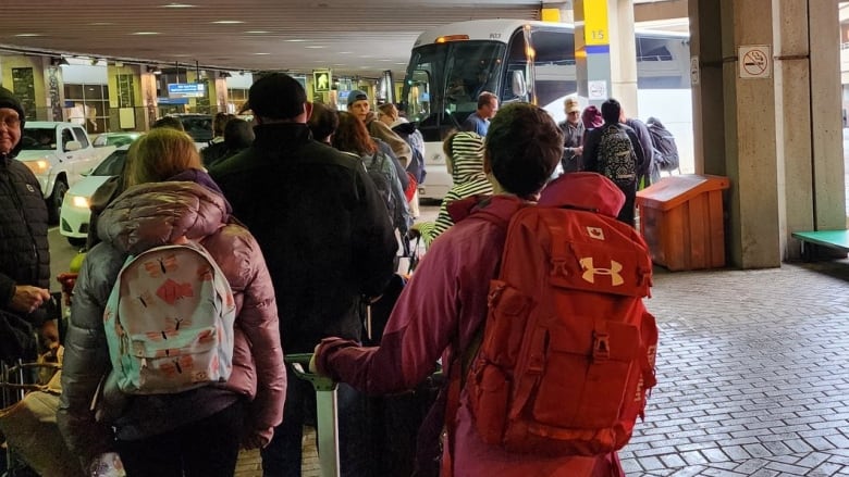 A crowd of people in jackets line up in front of a large bus.