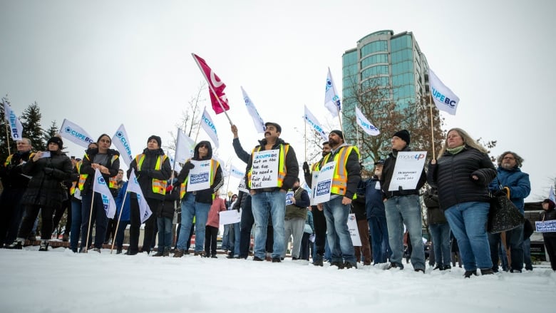 A group of workers holding picket signs stands in a snowy parking lot.