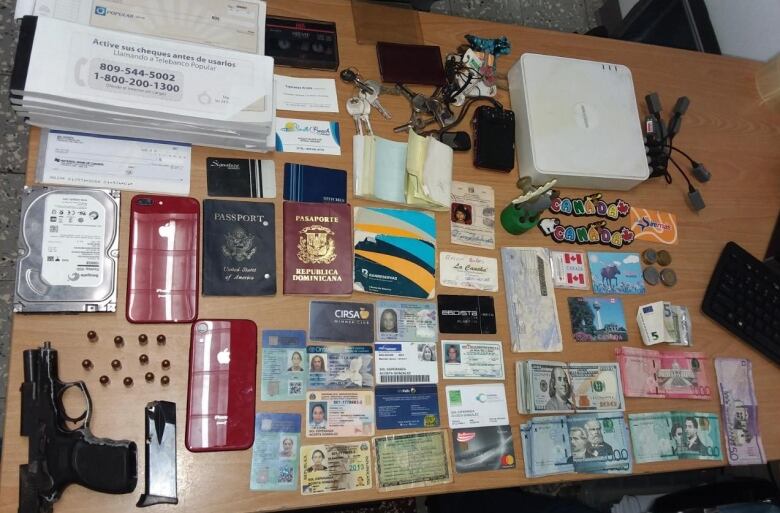 Table covered with things seized from a fraudster including a gun, passports, IDs and cash.